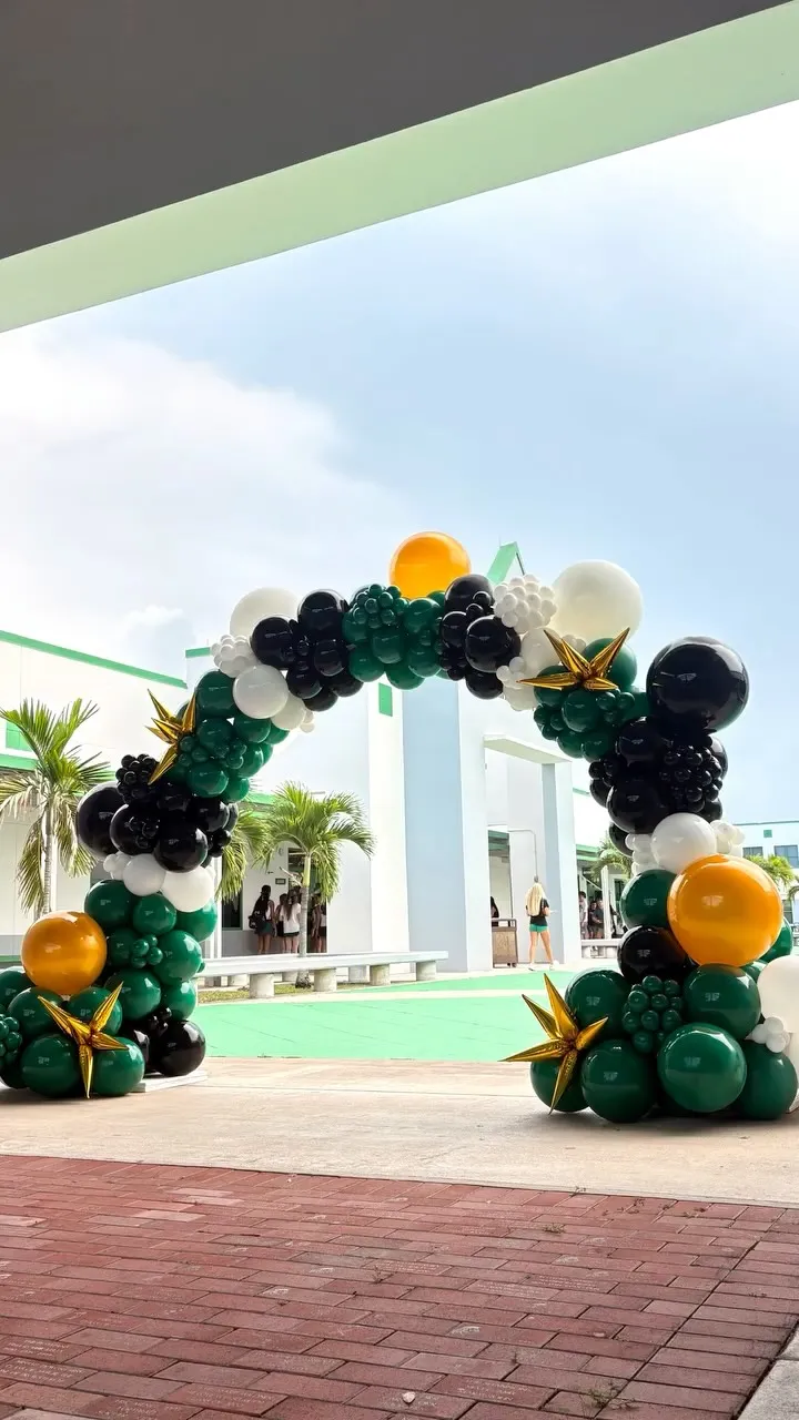 Outdoor balloon arch in green, black, white and gold at a school entrance
