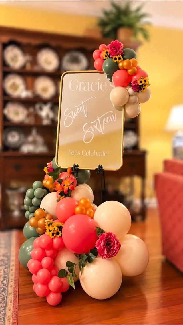 Welcome sign on an easel dressed with coral, sage and cream balloons and flowers